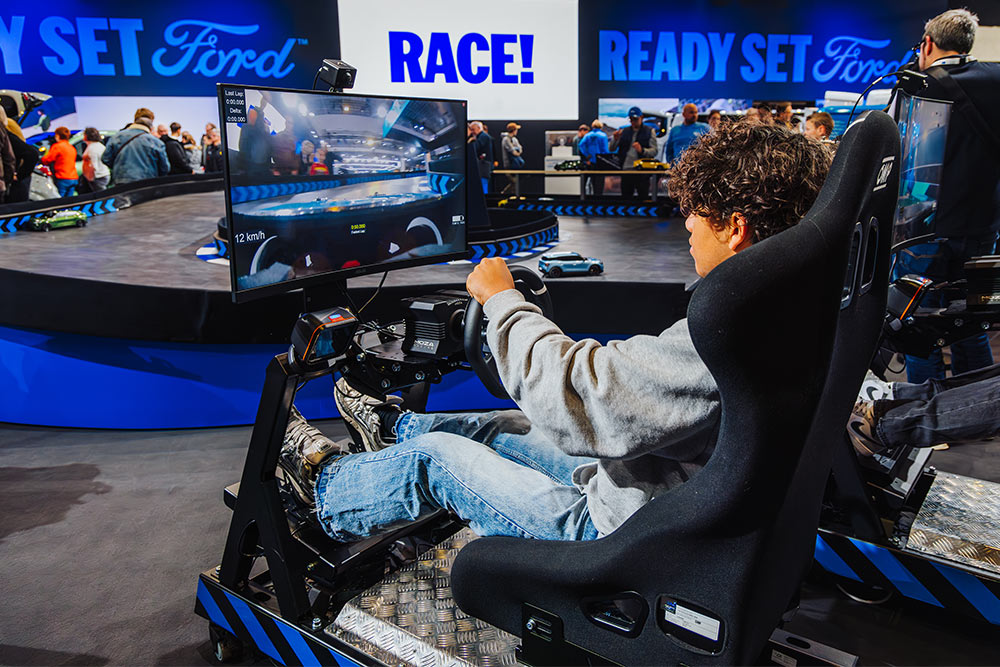 Un visiteur joue sur un simulateur de course virtuel sur un stand Ford à l'éclairage moderne.