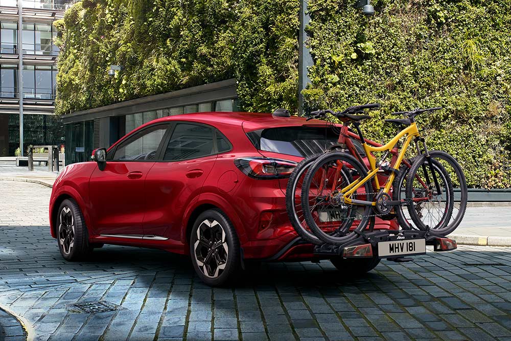 Ford Puma rouge stationné dans un cadre urbain avec deux vélos montés sur un porte-vélos arrière.