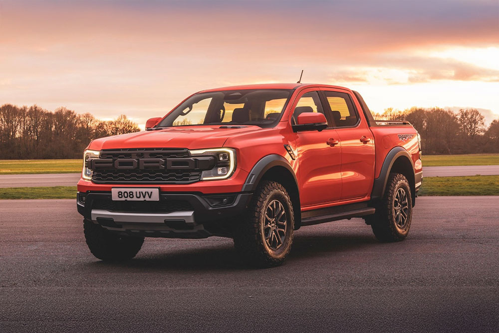 Un pick-up Ford Ranger Raptor orange garé au milieu d'un décor pittoresque.