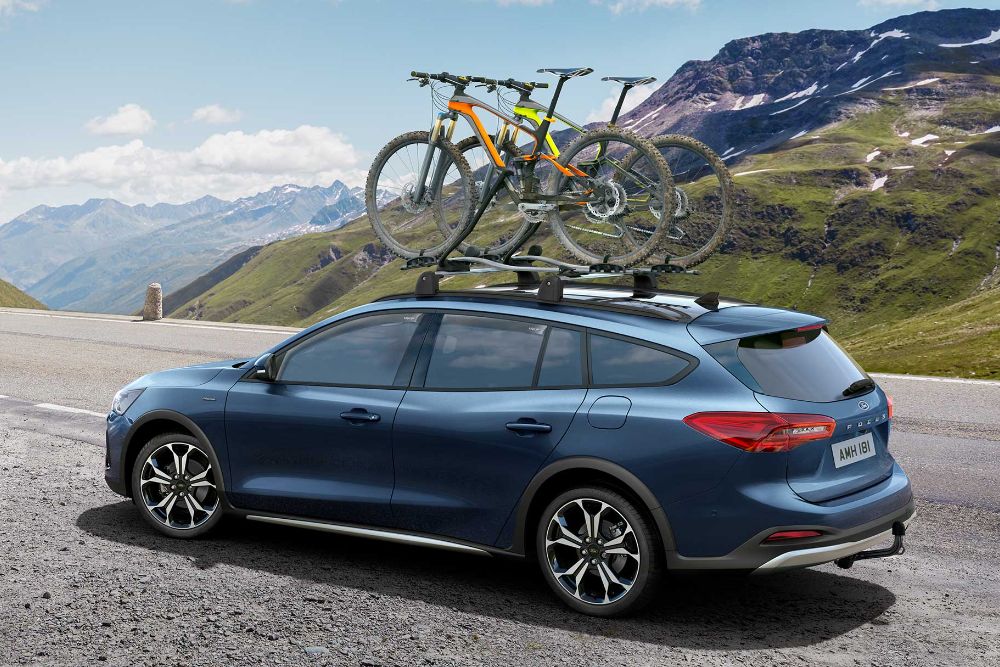 Ford Focus, couleur bleue, roulant sur une route de montagne avec déflecteurs et pare-soleil. Vue arrière aux trois quarts.