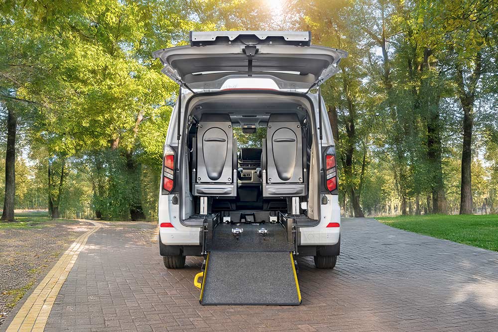 Vue arrière d'un Ford Transit Custom blanc avec un hayon ouvert et une rampe pour fauteuil roulant déployée.
