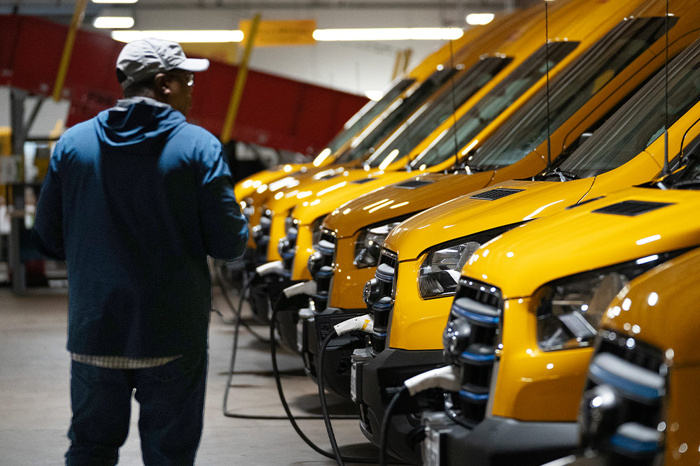 Une rangée de fourgons électriques Ford jaunes en charge, un homme se tient à côté d'eux.