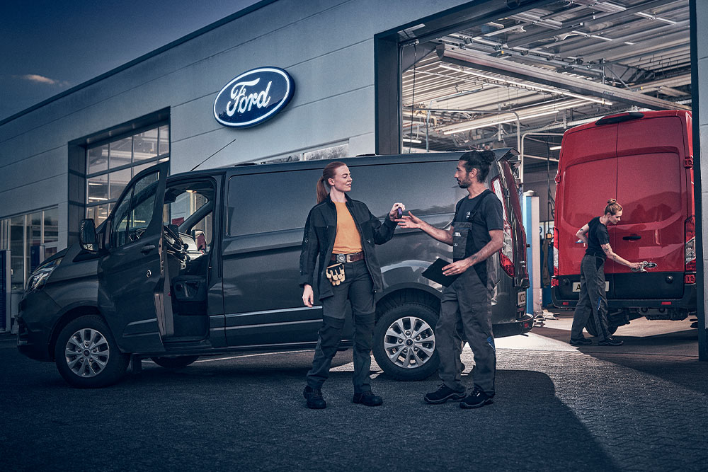 Client et technicien Ford échangeant les clés d'une camionnette devant une concession Ford.