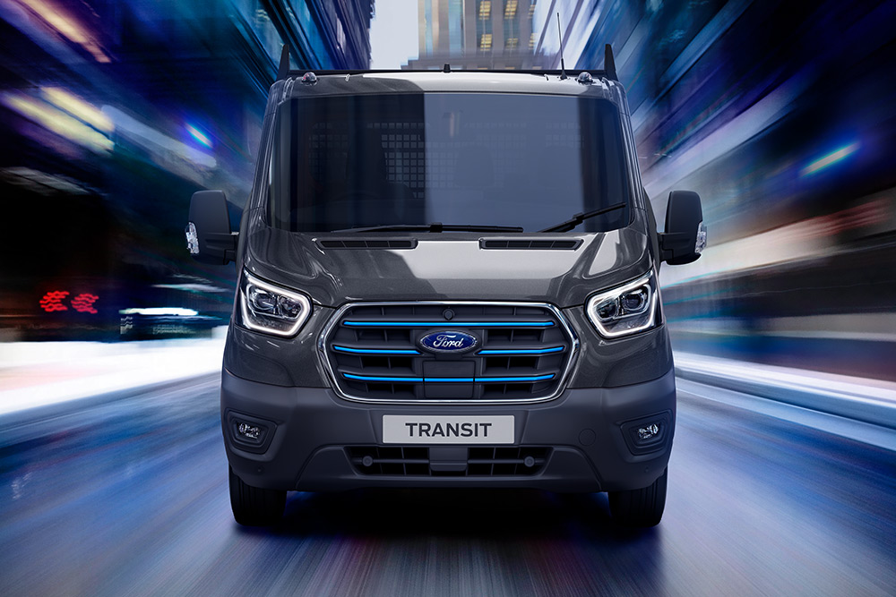 Un Ford Pro Transit argenté garé sur un chantier de construction, avec des ouvriers du bâtiment en arrière-plan.