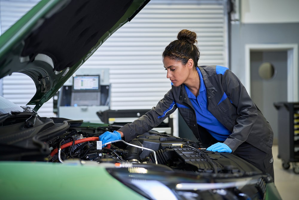 Une mécanicienne inspecte le moteur d'une voiture Ford sous le capot ouvert dans un atelier